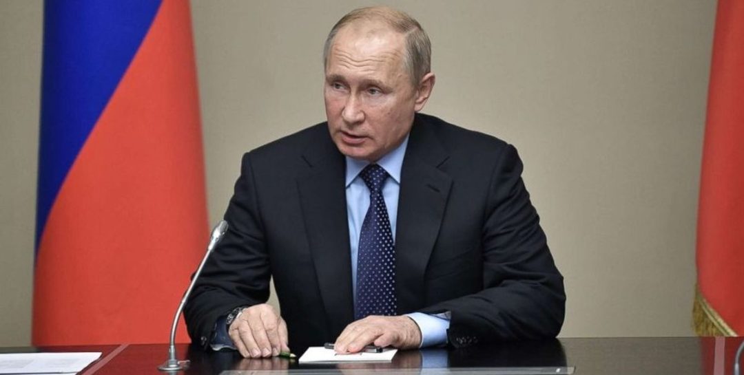 נשיא רוסיה, ולדימיר פוטין יושב על שולחן ומביט ימינה